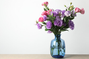 Vase with beautiful eustoma flowers on wooden table, space for text