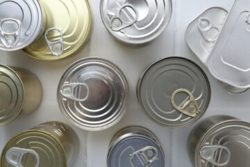 Many closed tin cans on white tiled table, flat lay