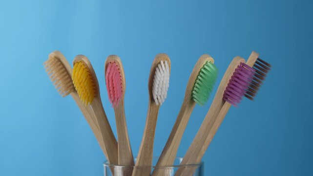 Set of colorful bamboo toothbrushes in glass on blue background, close up, rotates. Zero waste, plastic free, eco friendly organic product concept