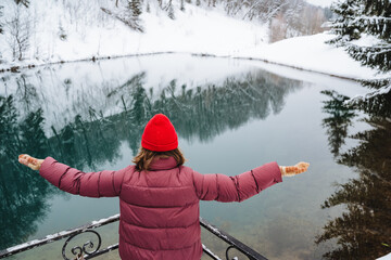 A woman is joyfully embracing the beauty of nature while standing beside a serene winter lake,...