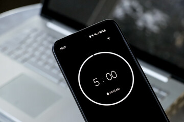 A phone with a black and white 5-minute timer to study with pomodoro method on laptop keyboard,...