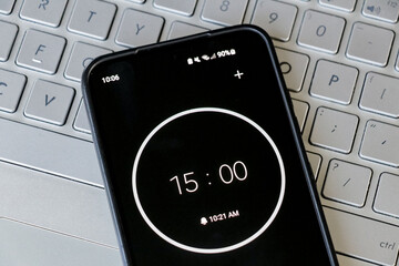 A phone with a black and white 15-minute timer to study with pomodoro method on laptop keyboard, study business background