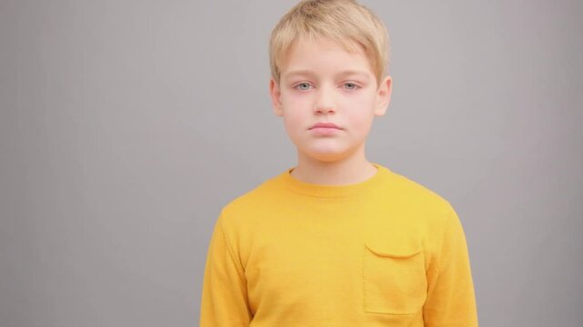 A boy in a yellow T-shirt on a gray background winks and smiles.