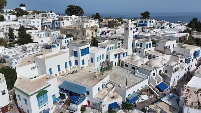 Scenic drone footage of Sidi Bou Said in Tunisia, capturing its iconic blue doors, whitewashed walls, cobblestone paths, and sweeping Mediterranean coastal views on a sunny day.