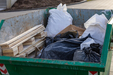 Construction waste and garbage in a green dumpster on an outdoor construction site with wood...