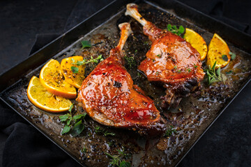 Traditional barbecue gourmet duck haunch with orange slices and herbs served as close-up on a rustic metal tray