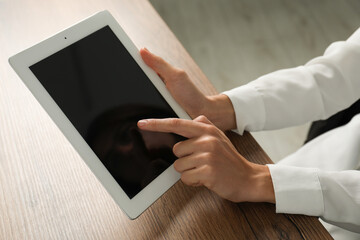 Businesswoman using tablet at wooden table indoors, closeup. Modern technology