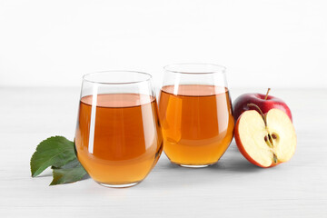 Fresh apple juice in glasses, fruits and green leaves on white wooden table