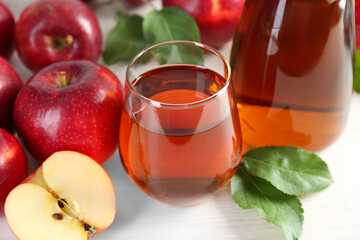 Fresh apple juice, fruits and green leaves on white wooden table, closeup
