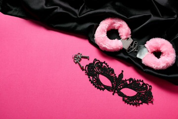Fluffy handcuffs, keys, lace mask and black fabric on pink background, flat lay. Space for text