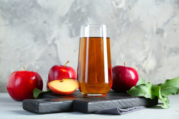 Fresh apple juice in glass, fruits and green leaves on light grey table