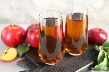 Fresh apple juice in glasses, fruits and green leaves on light grey table, closeup