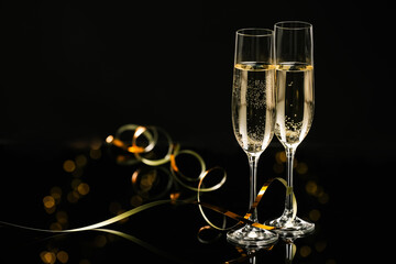 Champagne in glasses and party streamers on black mirror surface, space for text