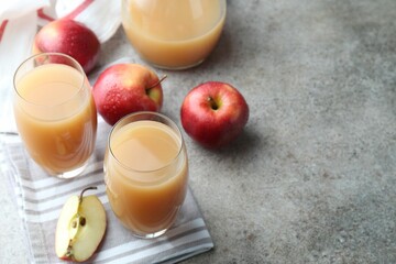 Refreshing apple juice in glasses and fruits on grey textured table. Space for text