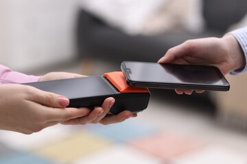 Woman paying with smartphone via terminal against blurred background, closeup