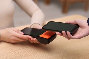 Woman paying with smartphone via terminal at wooden counter indoors, closeup