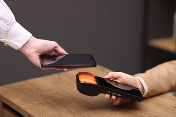Woman paying with smartphone via terminal at wooden counter indoors, closeup