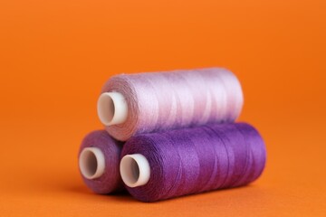 Spools of colorful sewing threads on orange background, closeup