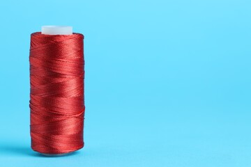 Spool of red sewing thread on light blue background, space for text