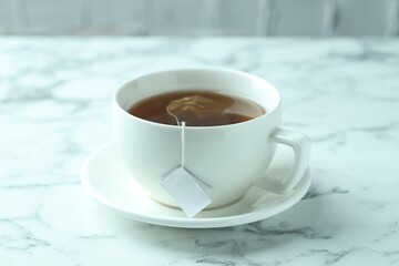 Tea bag in cup with hot drink on light marble table