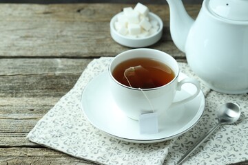 Tea bag in cup with hot drink, teapot and spoon on wooden table. Space for text