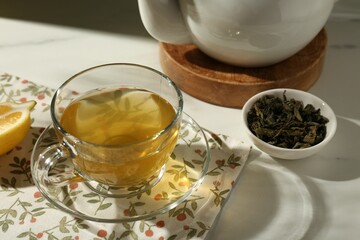 Refreshing green tea in cup and dry leaves on white table, closeup