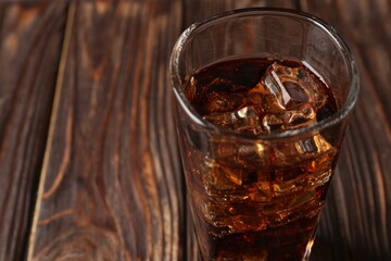 Cold cola with ice cubes in glass on wooden table, closeup. Space for text