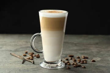 Tasty latte macchiato in glass cup, coffee beans and vanilla pods on grey table, closeup