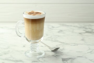 Tasty latte macchiato in glass cup on white marble table, closeup. Space for text