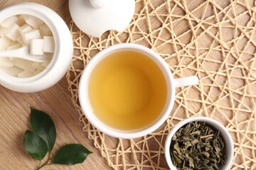 Refreshing green tea in cup, sugar bowl and leaves on wooden table, flat lay