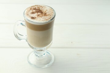 Tasty latte macchiato in glass cup on white wooden table, closeup. Space for text