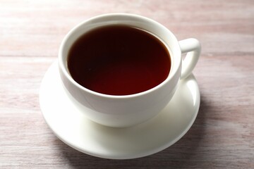 Refreshing black tea in cup on light wooden table, closeup