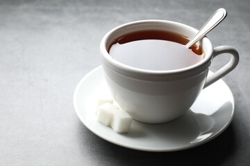 Refreshing black tea in cup and sugar cubes on grey textured table, closeup. Space for text