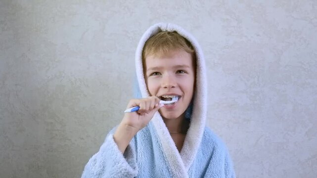 A child brushes his teeth. Children's toothbrush and toothpaste. A little boy in a blue robe brushes his teeth and laughs, fooling around. Oral hygiene and children's health.