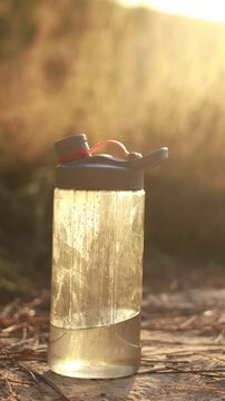 A close-up of a reusable water bottle filled with fresh water, sitting on a wooden surface with a warm, sunlit background.