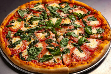 A pizza with tomatoes, cheese and basil on a metal pan