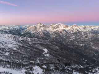 Fototapeta premium Serene peaceful aerial of snow covered peaks Italian Alps in pink morning clear blue skies