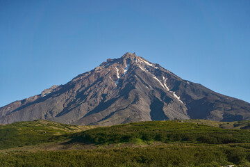 Koryaksky volcano. This is a truly stunning view of a magnificent volcano, surrounded by rugged terrain and clear blue skies