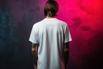 Fototapeta premium A person with long hair stands with their back to the camera, wearing a plain white t-shirt mockup. The background features a gradient of pink and blue hues, creating a vibrant atmosphere.