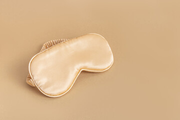 Golden silk sleep mask on beige background. A sleep accessory