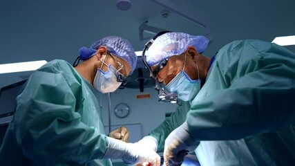 Two surgeon co-work at maxillofacial surgery. Attentive doctors in surgical loupes carefully use the instruments. Low angle view.