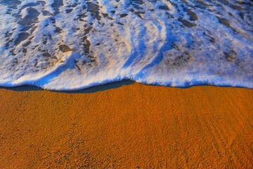 Sea waves with foam and sandy beach in golden sunset at a coastline