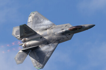 Close top view of a F-22 Raptor in beautiful light in a turn, with condensation clouds at the wing...