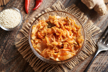 Fermented kim chi in a bowl on a table with chilli peppers, sesame seeds and ginger