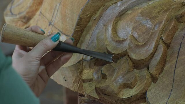 Hands of craftsperson making artistic carvings on wood close-up.