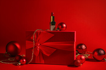 Christmas present. Lipstick, gift box and festive decor on red background
