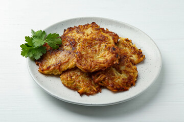 Delicious potato pancakes and parsley on white wooden table, closeup