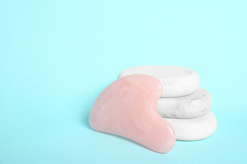 Rose quartz gua sha tool and spa stones on light blue background. Space for text