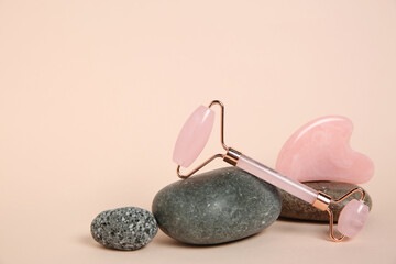 Face roller, gua sha tool and stones on beige background. Space for text