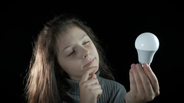 Inspired preteen with bulb. A view of preschool girl have an idea and hold the bulb in her hands on black .